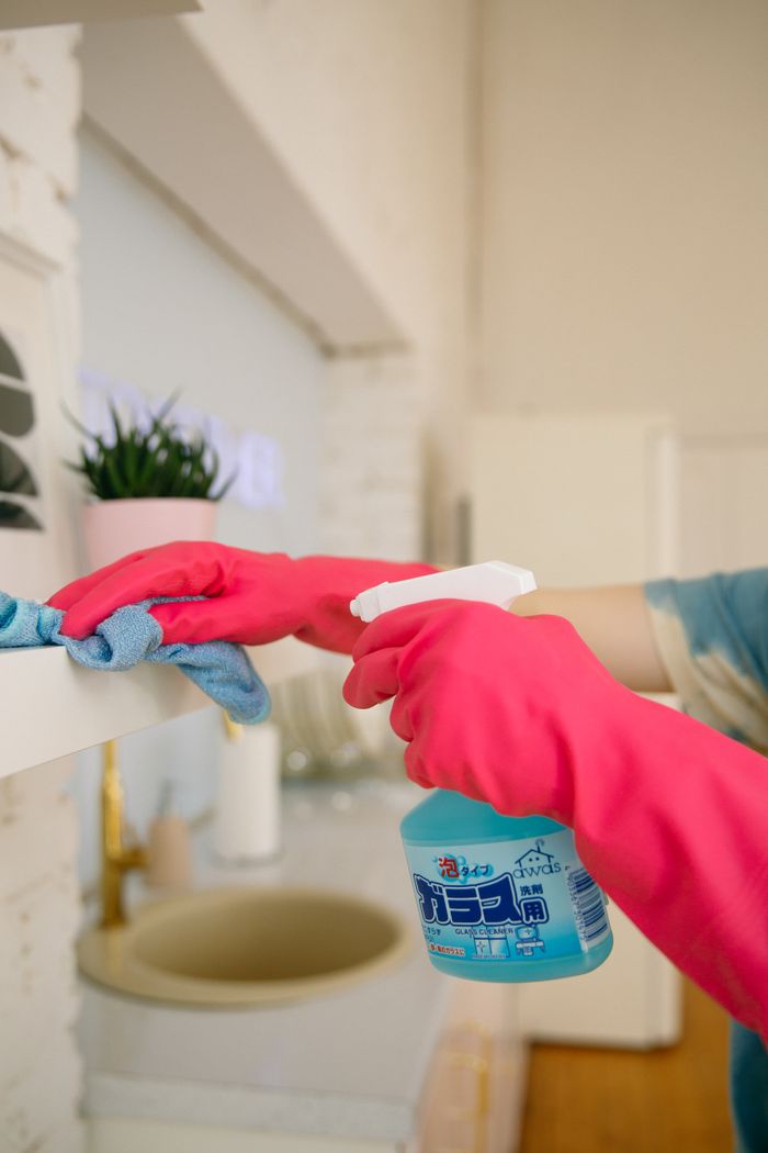 A person uses a spray bottle and cloth to clean a kitchen shelf, helping maintain hygiene and cleanliness.