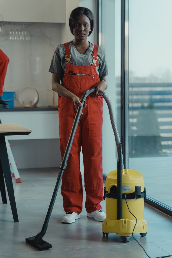 Une femme adulte vêtue d'une combinaison rouge utilise un aspirateur dans un intérieur moderne, concentrée sur les tâches de nettoyage.